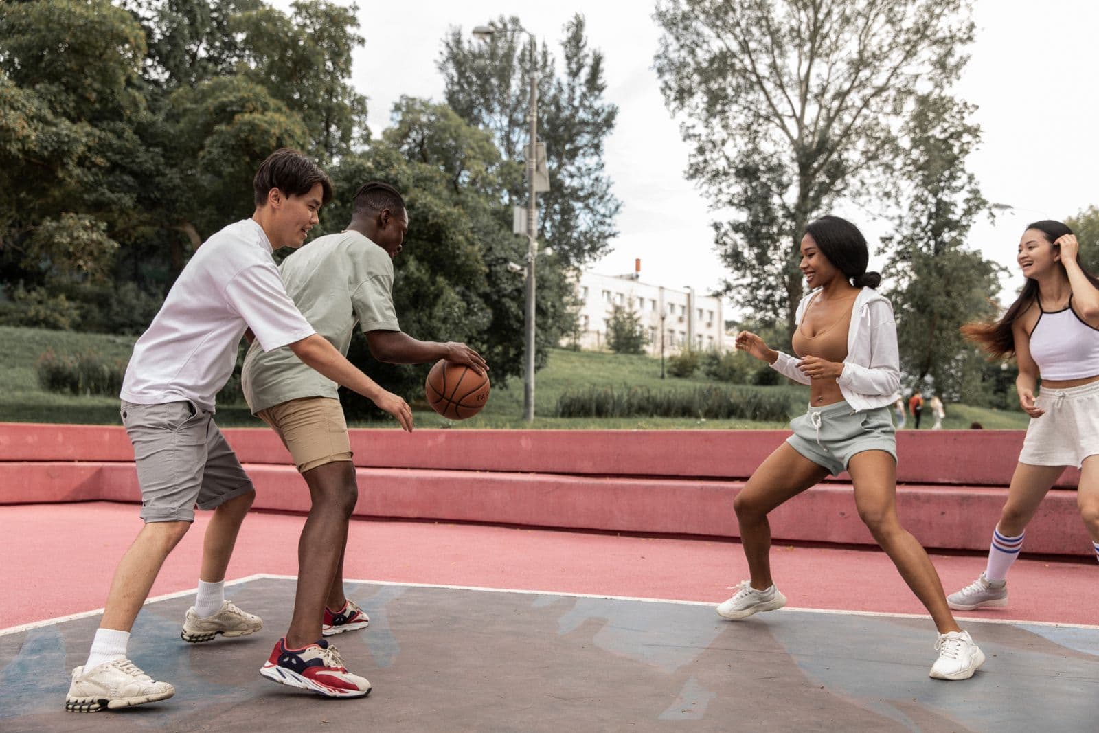 A diverse group of young friends playing a lively pickup basketball game together on an outdoor park court on a sunny day