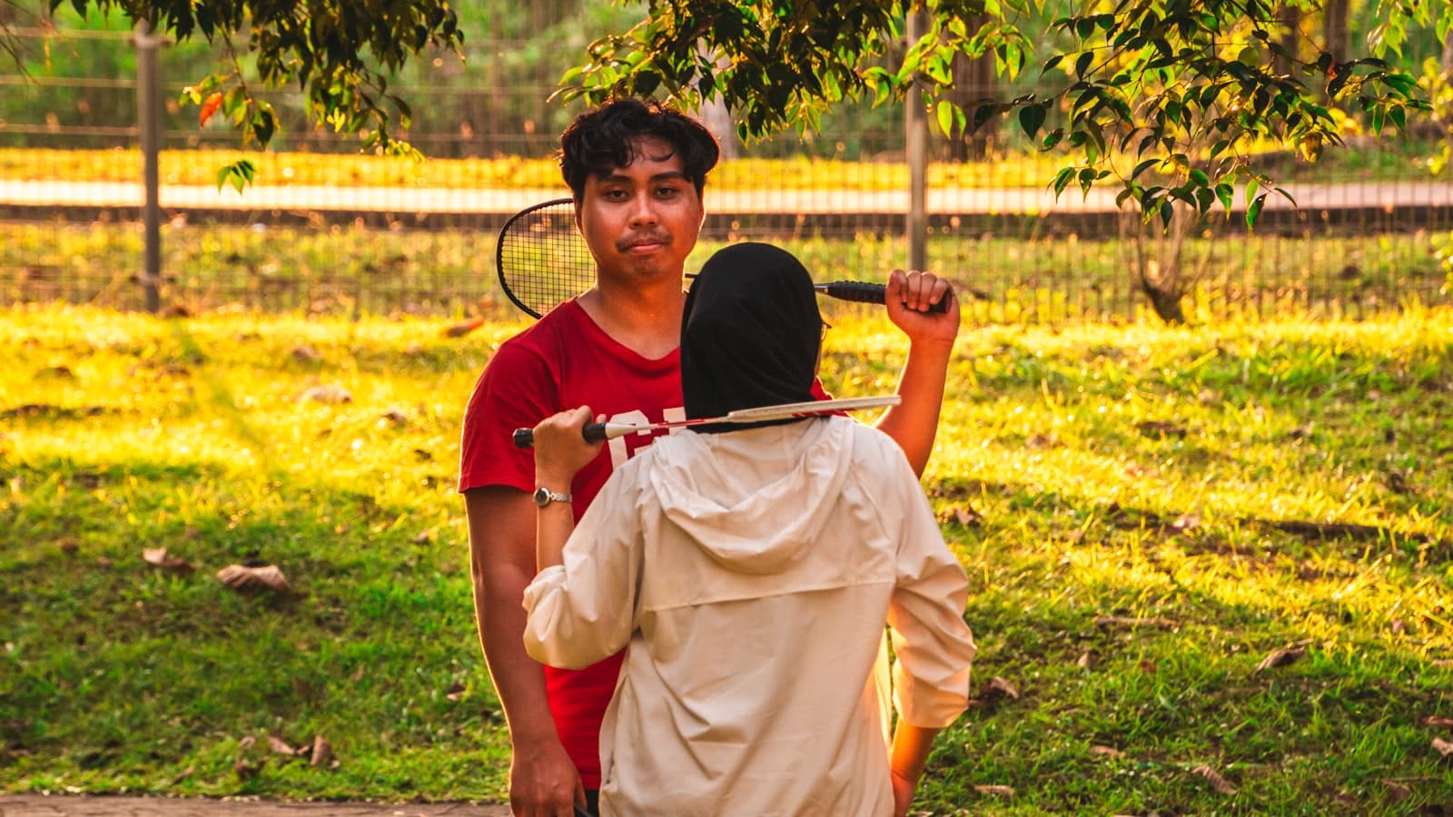 Two people playing badminton together in a park at sunset