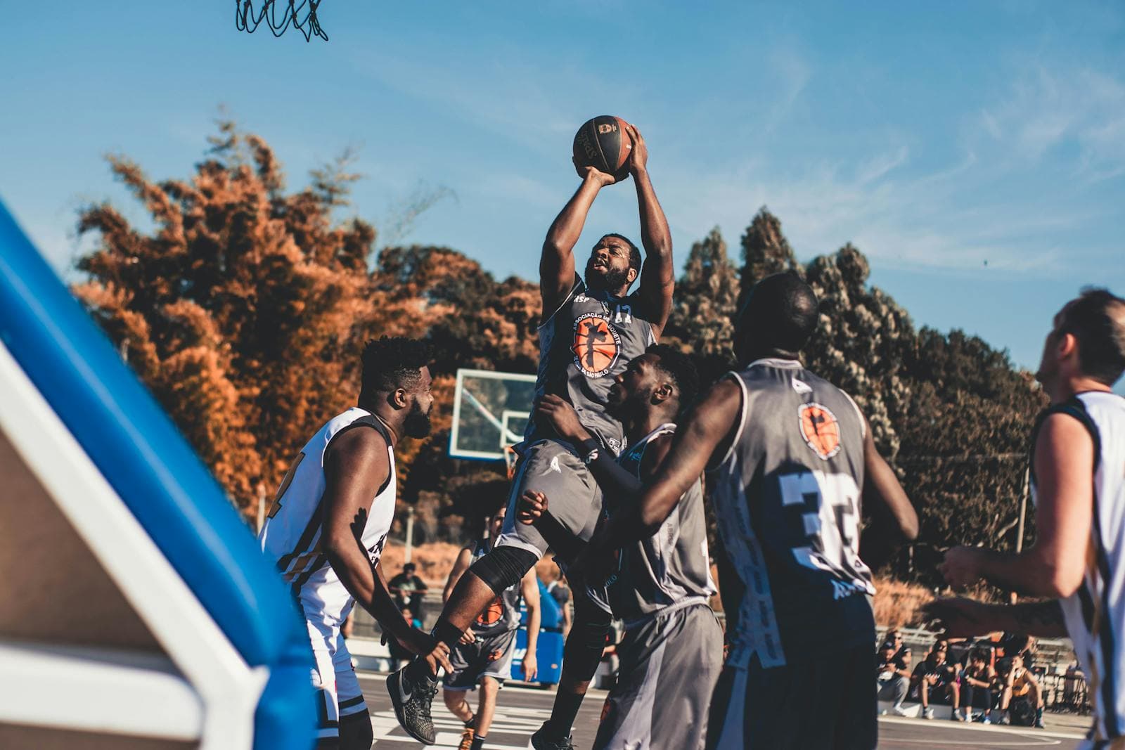 A competitive outdoor pickup basketball game, one player rising up for a shot among defenders on a park court