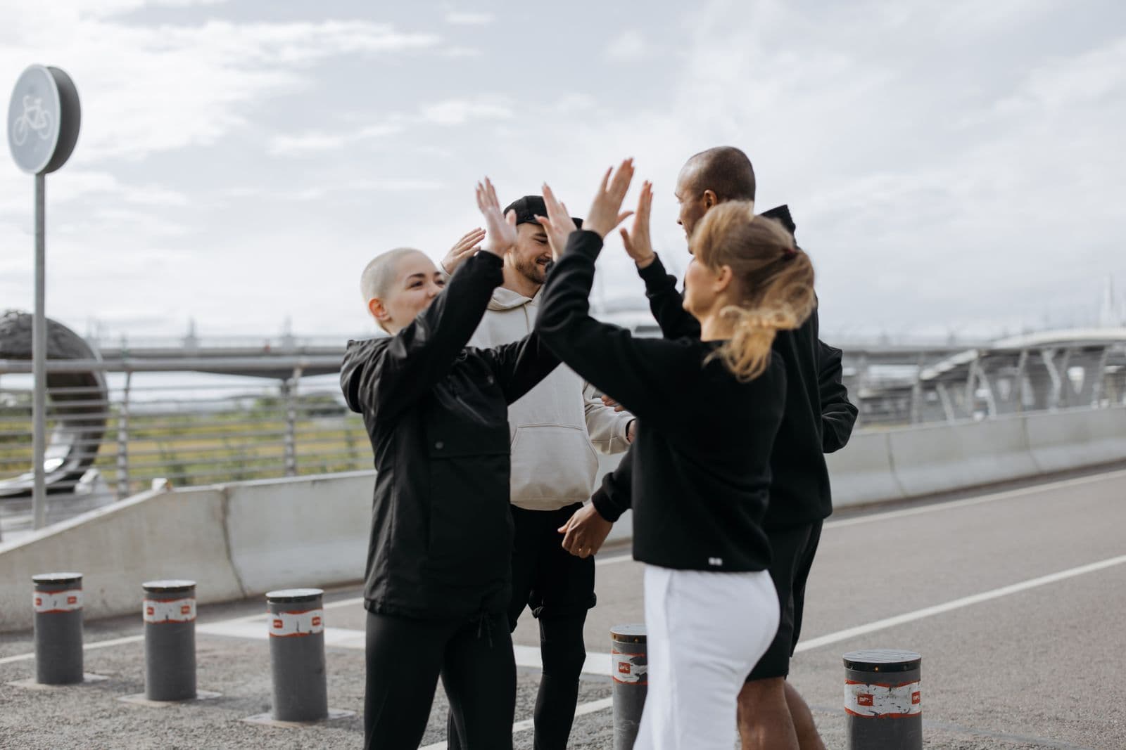 A diverse group of friends in athletic wear celebrating with a group high-five outdoors after a workout