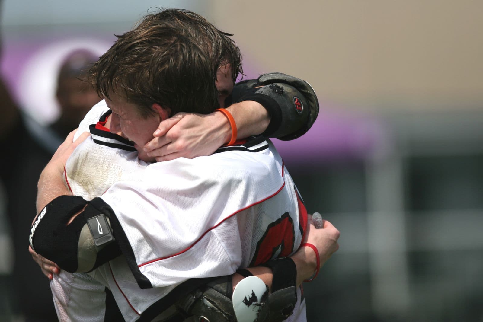 Two amateur lacrosse players sharing an emotional embrace after a game, communicating everything without a single word