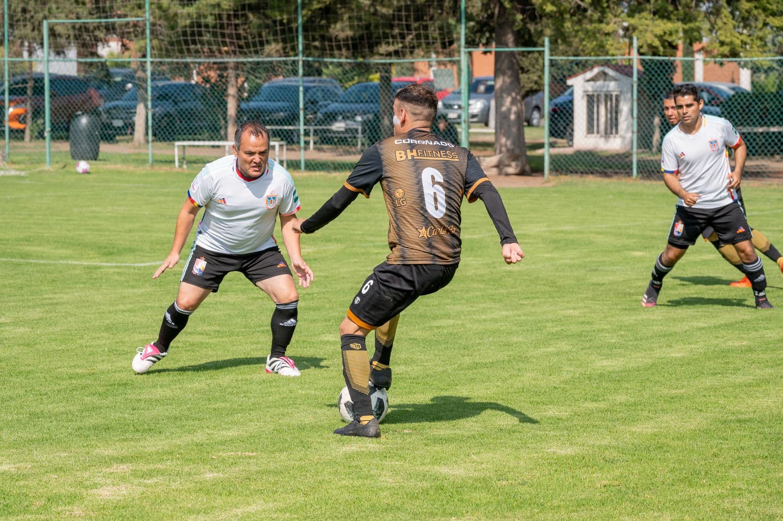 Adults playing a casual recreational soccer match on a grass field, one player shielding the ball from a defender